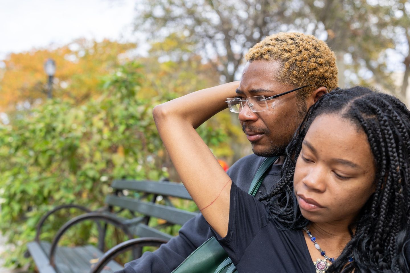 Woman reaching back to touch the man's face while they sit together on a park bench