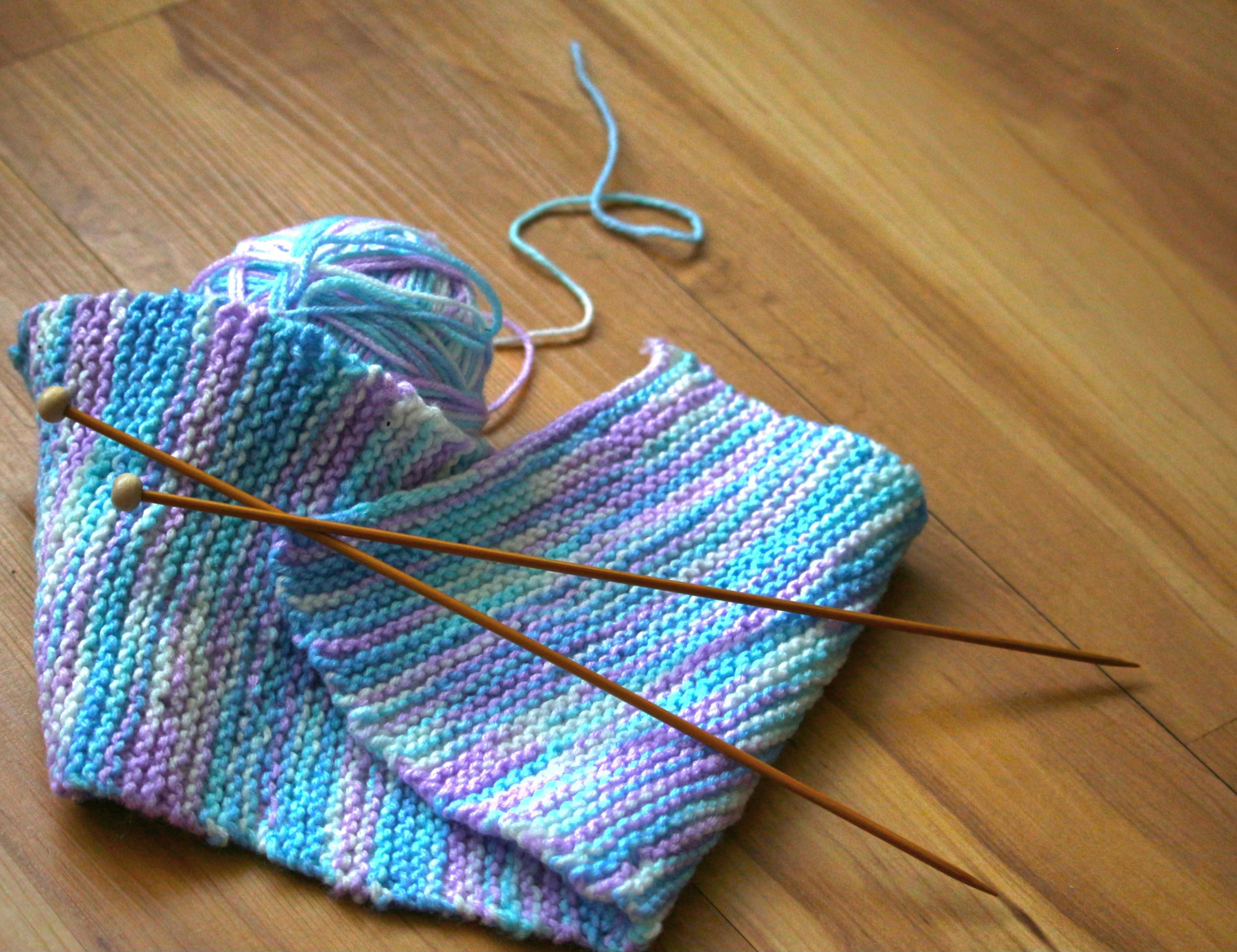 Multi-colored ball of yarn, knitting needles, and knitted piece on floor