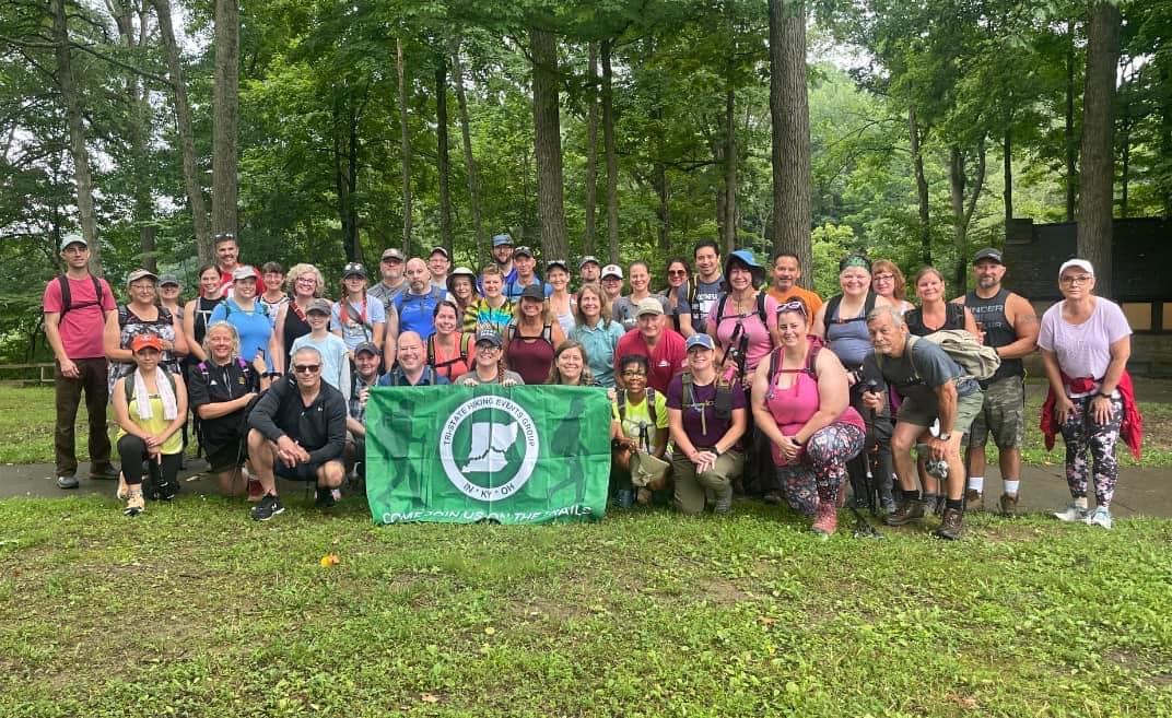 Tri-State Hiking large group holding a group banner with their logo outside at a park