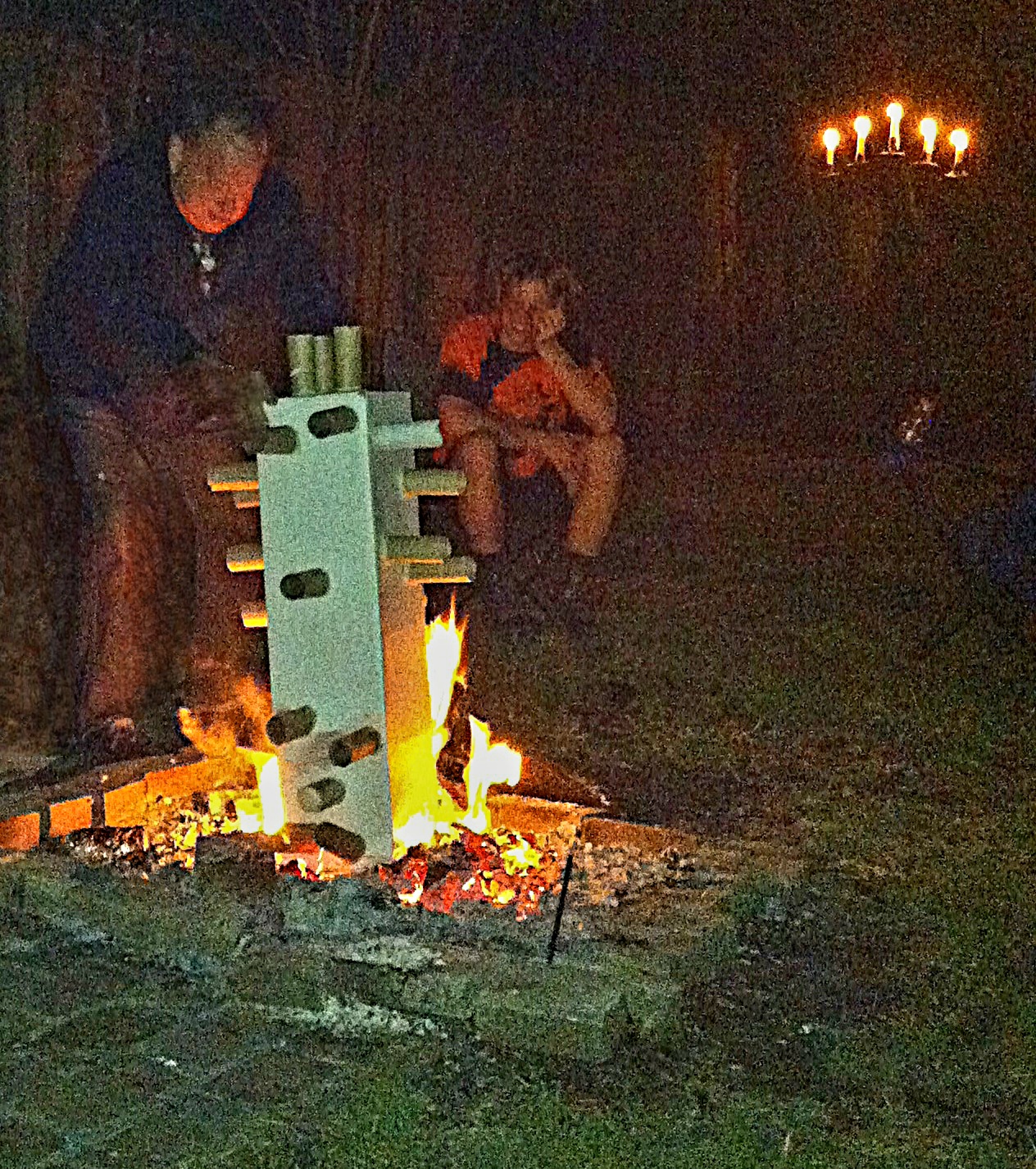 Man placing onto a fire  a tall box  with multiple cardboard tubes poking out of it.