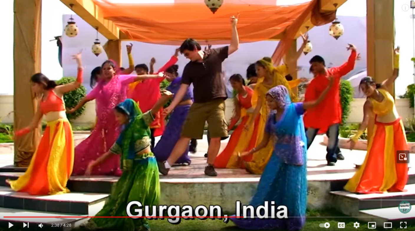 Young, white male dancing with Bollywood dancers in India who are colorful sarees