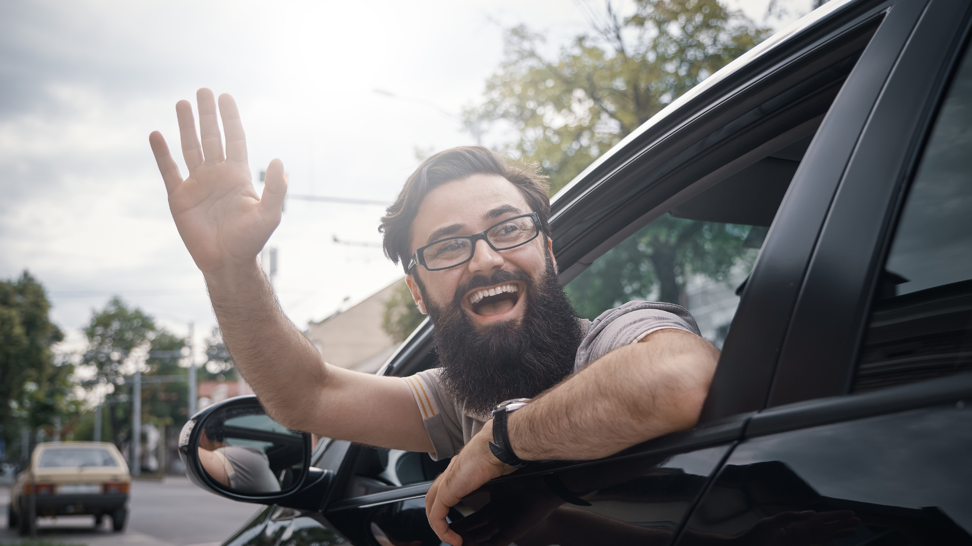 A man joyfully waving from his car window