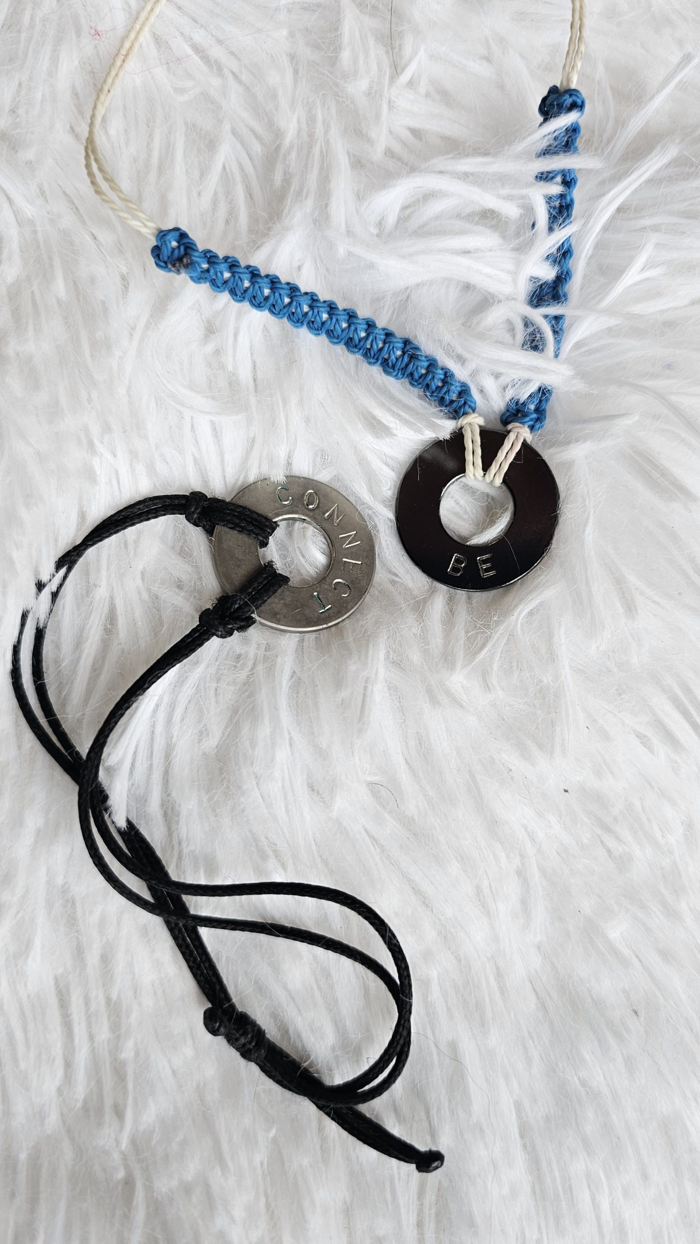 Two intention bracelets with circular metal rings with words inscribed; one says "be" and the other says "connect."