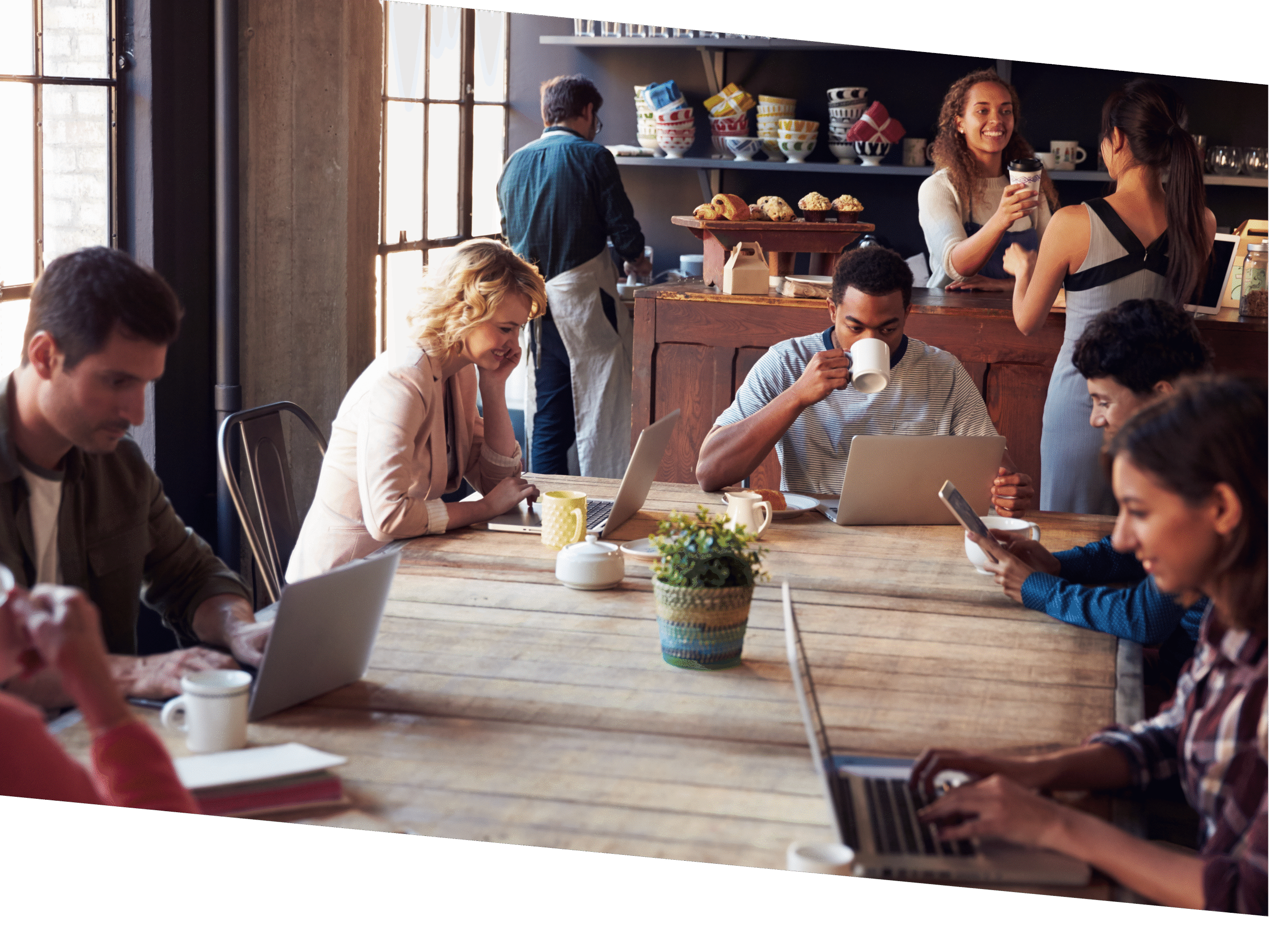 People gathered around a shared table at a coffee shop, many are working on their laptops.