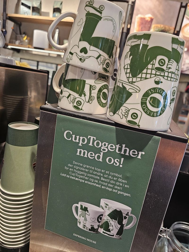 090225 CupT04 CupTogether sign with green cups in a coffee shop in Copenhagen. Language is Danish on the sign.